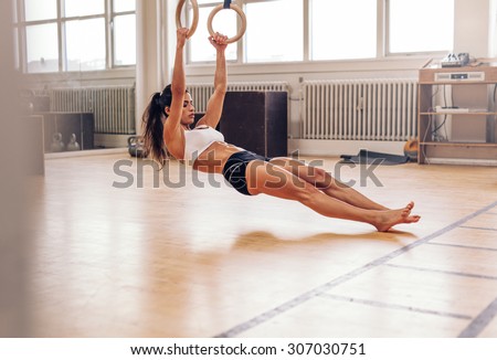 Young fit woman pulling up on gymnastic rings. Muscular woman exercising on gym.