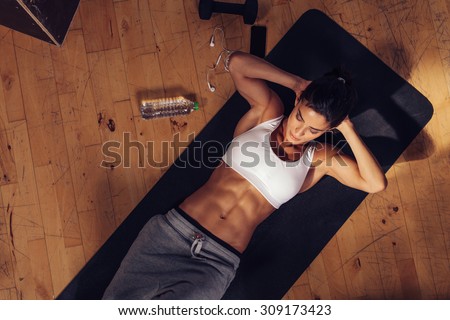 Sporty young woman lying on yoga mat doing sit-ups in gym. Top view of muscular woman doing abs crunches.