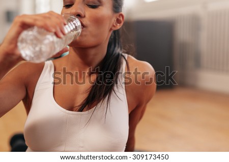Close up shot of fitness woman drinking water in a break. Young female at gym taking a break after fitness training.