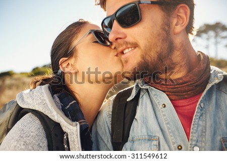Loving young tourist couple hiking. Young woman kissing cheek of her boyfriend, outdoors on a hike.