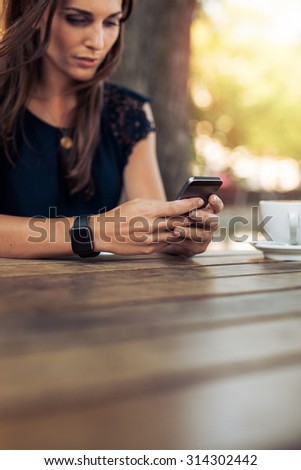 Cropped image of young female reading a text message on her smart phone. Woman using smart phone in a outdoor cafe.