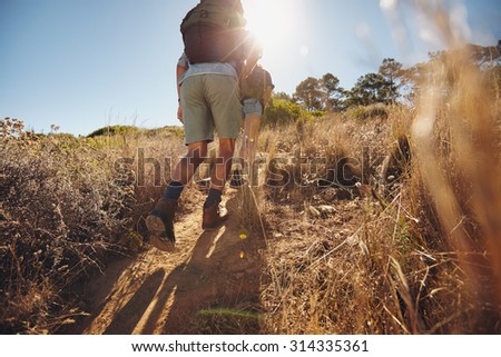 Low angle view of two young people climbing uphill on a mountain. Couple on a hiking trip on a sunny day.
