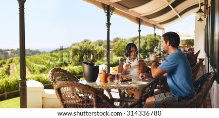 Couple enjoying a glass of wine in a vineyard. Young man and woman drinking white wine while sitting at a table on a wine cellar.