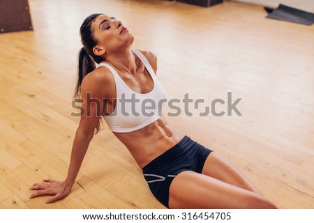 Portrait of tired woman having rest after workout. Tired and exhausted female athlete sitting on floor at gym.