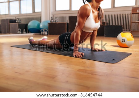 Cropped shot of young woman stretching her stomach on fitness mat. Muscular female doing stretching exercise in gym.