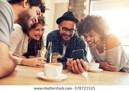 Portrait of cheerful young friends looking at smart phone while sitting in cafe. Mixed race people sitting at a table in restaurant using mobile phone. ストックフォト © 