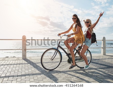 Joyful young women riding a bicycle together. Best friends having fun on a bike at the seaside promenade. Foto d'archivio © 