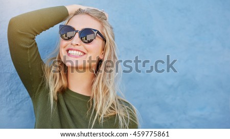 Photo of Close up shot of stylish young woman in sunglasses smiling against blue background. Beautiful female model with copy space.