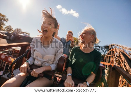 Young friends on thrilling roller coaster ride. Young women and men having fun at amusement park. 商業照片 © 