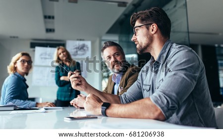 Photo of Young designer giving some new ideas about project to his partners in conference room. Business people discussing over new business project in office.