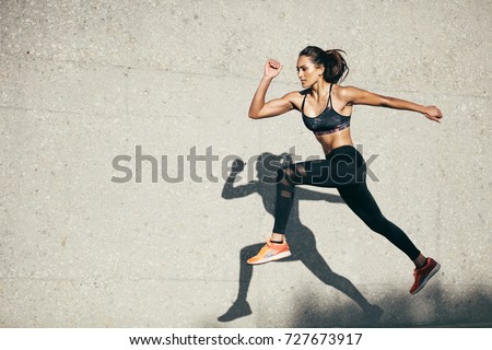 Young woman with fit body jumping and running against grey background. Female model in sportswear exercising outdoors. Stok fotoğraf © 