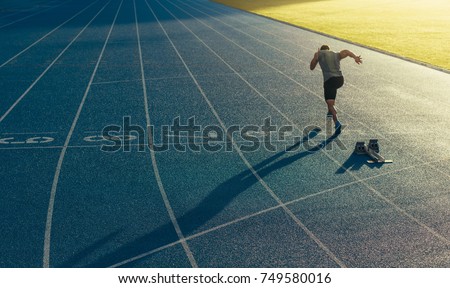 Athlete running on an all-weather running track alone. Runner sprinting on a blue rubberized running track starting off using a starting block. Foto d'archivio © 
