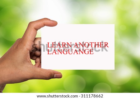 hand holding white card written learn another language over blur background