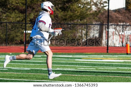 A high school boy lacrosse player is running doen the field with the ball in the net of his stick looking to make a play. Stockfoto © 