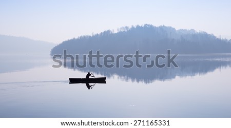 Man floating in a boat. Fog over the lake, mountains reflected in the water