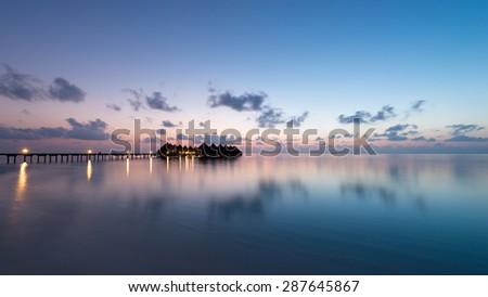 Panorama of tropical island.  Turquoise water lagoons, coral reefs visible. Sunrise sky and clouds painted in pink. Tourist Resort Deluxe. Maldives