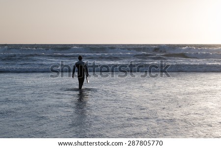 The male figure with a board for surf on a background of ocean waves. The setting sun paints the sky in bright orange, yellow, gold color. Vintage filter, monochrome