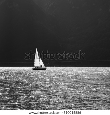 Sailing ship on the mountain lake. Sun reflected in water. Black and White