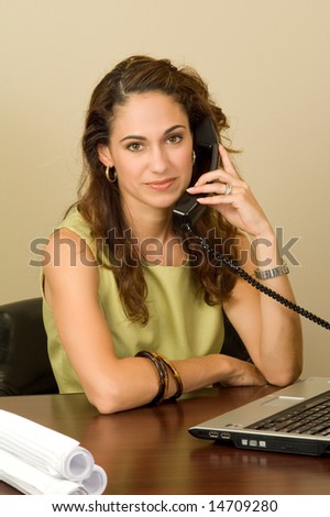 A pretty brunette business professional on the phone, wearing a green outfit.