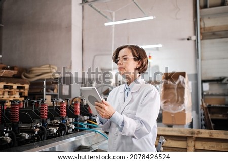 Portrait of female factory worker wearing glasses and white robe at polymer plastic manufacturing, using tablet for quality control and logistic purposes, checking machines and mechanisms 商業照片 © 
