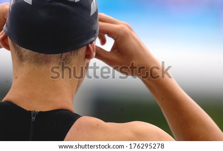 BUDAPEST, HUNGARY-AUGUST 04, 2006: Swimmer man with black swim cap holding goggles, seen from behind on starting blocks, during a race of teh European Swimming Championship in Budapest.