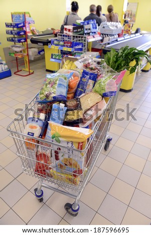 VARESE, ITALY-APRIL 11, 2014: Full shopping cart, and customers paying at the cash register of a supermarket, in Varese.