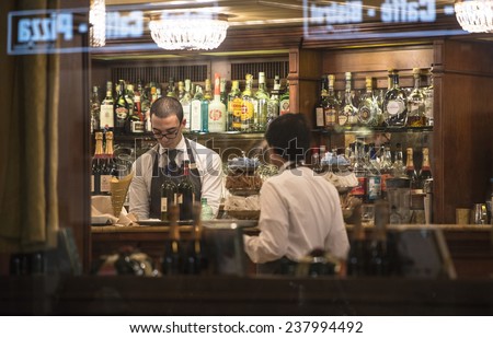 MILAN, ITALY-DECEMBER 02, 2014: barman at work on a traditional milanese bar, seen through the window at night, in Milan.