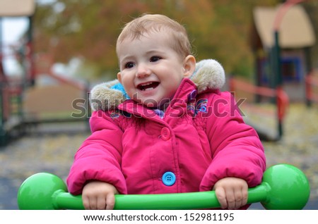 Young child, girl, having fun at the playground riding a green see-saw..