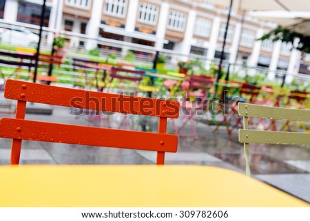Empty urban cafeteria or terrace with colorful chairs and tables, parasols and tile, outdoor, near a building, in summer. The weather is rainy