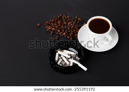 White cup of coffee with ashtray and coffee beans on the black background