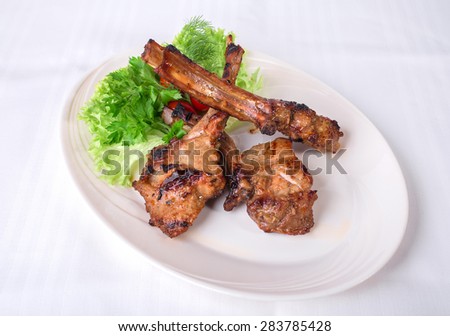 Delicious grilled lamb rack with fresh lettuce leaves. Plate located on a white canvas tablecloth background.