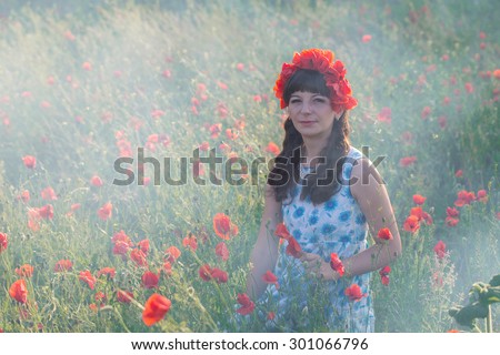 Beautiful romantic lady on the poppy field dressed in casual dress and floral wreath. Summer shot at sunset with haze.