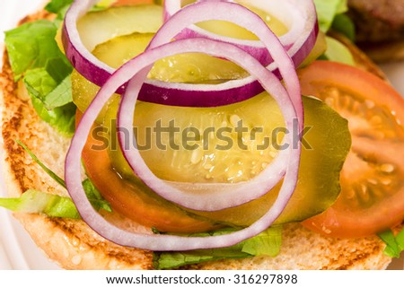 Closeup of burger bun with sliced red onion and pickled tomatoes on lettuce leaves. Macro. Photo can be used as a whole background.