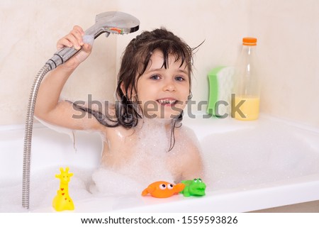 Beautiful toddler girl taking a bath in a bathtub with bubbles. Cute kid washing his hair with shampoo in the shower. 商業照片 © 
