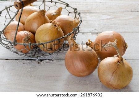 Yellow onions in a metal basket on a wooden table