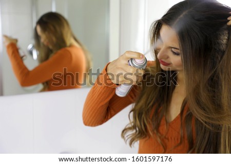 Young woman applying dry shampoo on her hair. Fast and easy way to keep hair clean with dry shampoo. Focus on the hand with spray.