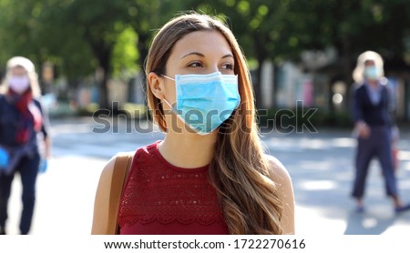 COVID-19 Social Distancing Woman in city street wearing surgical mask against disease virus SARS-CoV-2. Girl with face mask walks respecting social distancing during Pandemic Coronavirus Disease 2019.