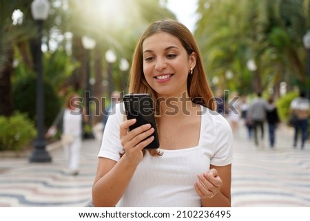 Excited young woman watching her smartphone when walking in the street with blurred people on the background. Millennial girl using mobile app outdoors. Teenager lifestyle technology concept. Foto stock © 