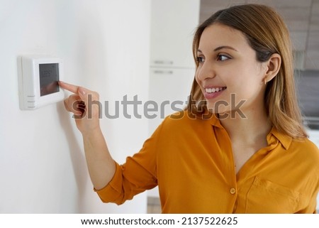 Portrait of smiling woman lowers the temperature on digital thermostat at home. Energy saving, efficient and smart technology. Сток-фото © 