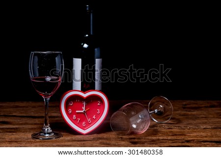 Glass of red wine with heart Clock on old brown wooden background