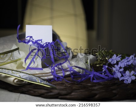 A heart gift box with shredded blue paper coming out of it and a blank note on it, it is next to blue flowers - homey & night feeling