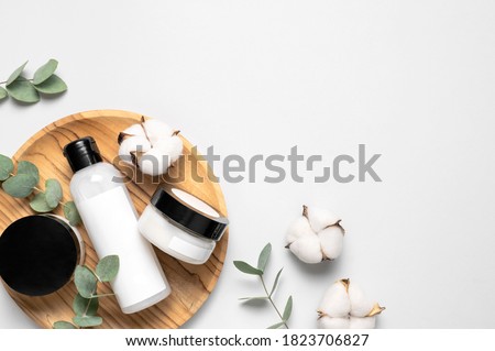 Natural organic eco cosmetics. Beauty SPA branding mock-up. Cosmetic containers with cream and lotion, cotton flowers, eucalyptus leaves on gray background flat lay top view. Blank label for branding