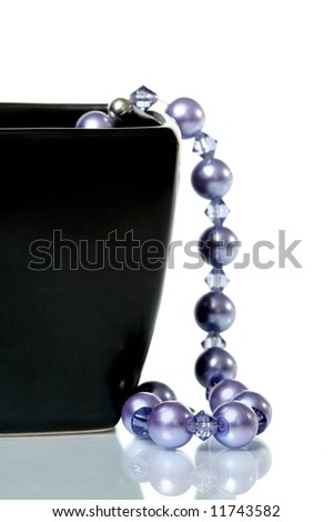 Purple necklace hanging from black glass bowl on white background