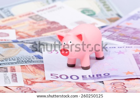 Toy pink pig standing on Euro, Russian rubles and dollars