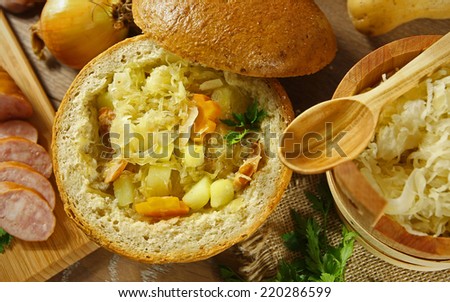 Cabbage soup in a loaf of bread and vegetables on a wooden table