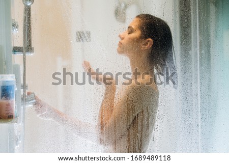 Morning shower.Taking rejuvenating cold shower.Self care moment.Everyday personal hygiene.Unfocused woman showering in glass shower with strong pressure water stream.Focus on drops