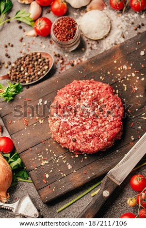 Round ground beef portioned beef patty made from beef mince on a wooden board. Hamburger meat seasoned and ready for a barbecue.Spices and condiments for a grill.Homemade burger recipe.Prepared burger