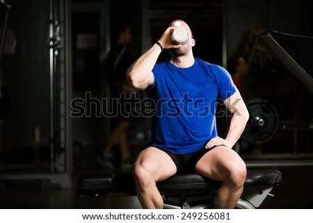 Handsome attractive muscular man after training in the gym.Young muscular man drinking protein shake on Scott bench after doing exercises