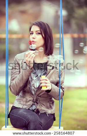 Beautiful woman blowing bubbles toned with a retro vintage instagram filter.Young woman blowing bubbles swinging in the park.Gorgeous flirty brunette woman starts soap bubbles in park