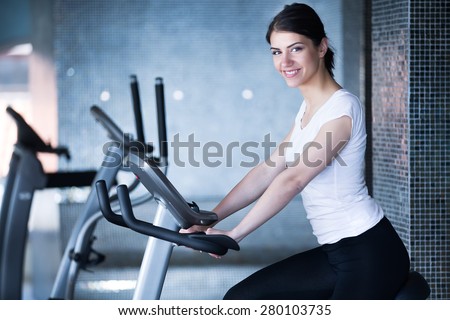 Woman riding an exercise bike in gym.Doing sport biking in the gym for fitness.Cardio and fat loss workout in the gym.Athletic woman pedaling on a stationary bike.Sport and fitness,summer body goals